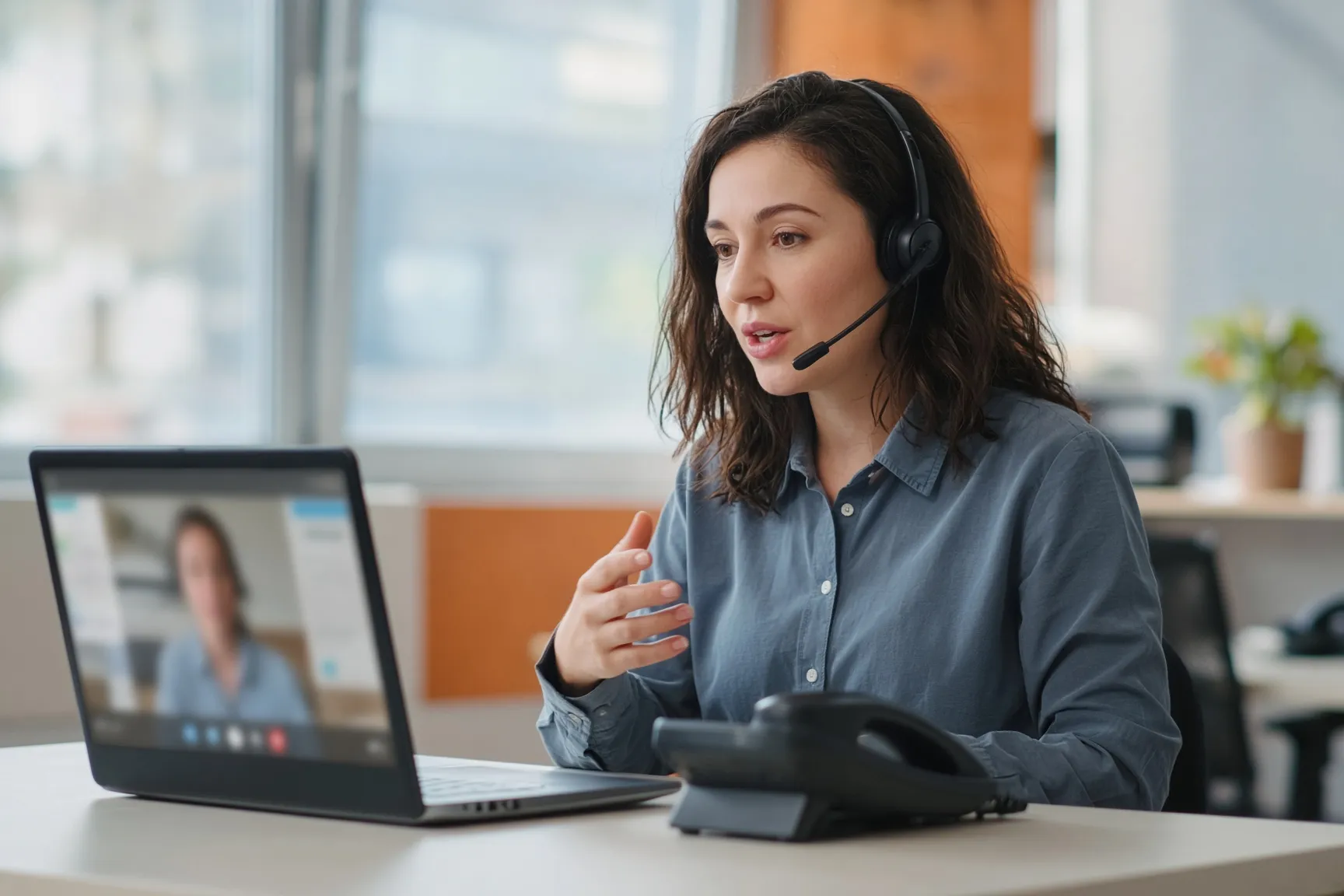 A person wearing a headset on a video call at their desk, with a desk phone nearby